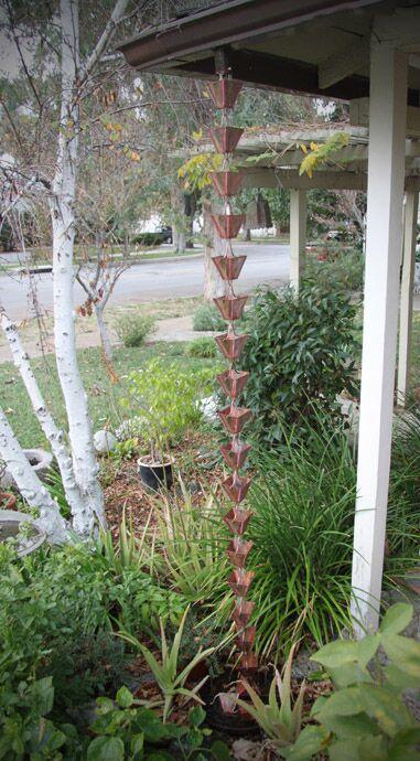 Full view of aged copper patina rain chain in a lush garden setting.