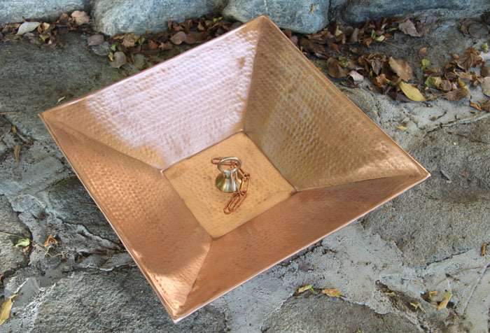 Copper rain chain basin with hammered finish placed outdoors on a stone surface.
