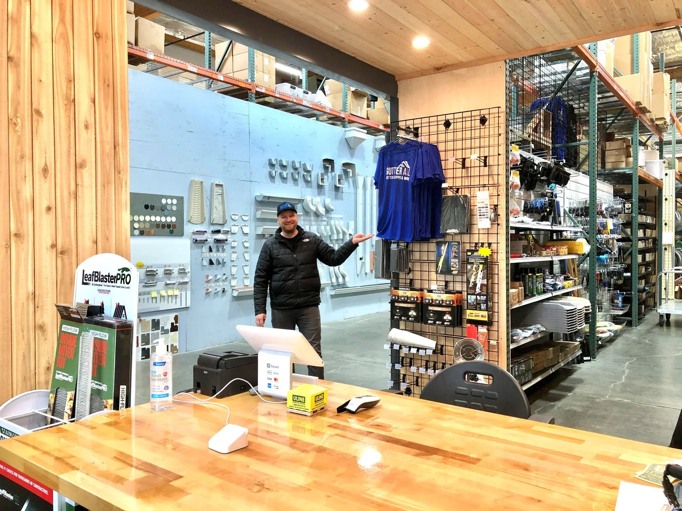 GutterAll Lake Oswego retail store interior with gutter accessories display wall, checkout counter, and owner greeting customers in Portland area showroom
