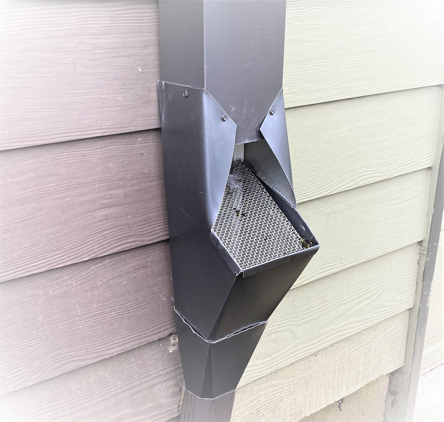 Black GutterAll downspout cleanout screen installed on a house wall.
