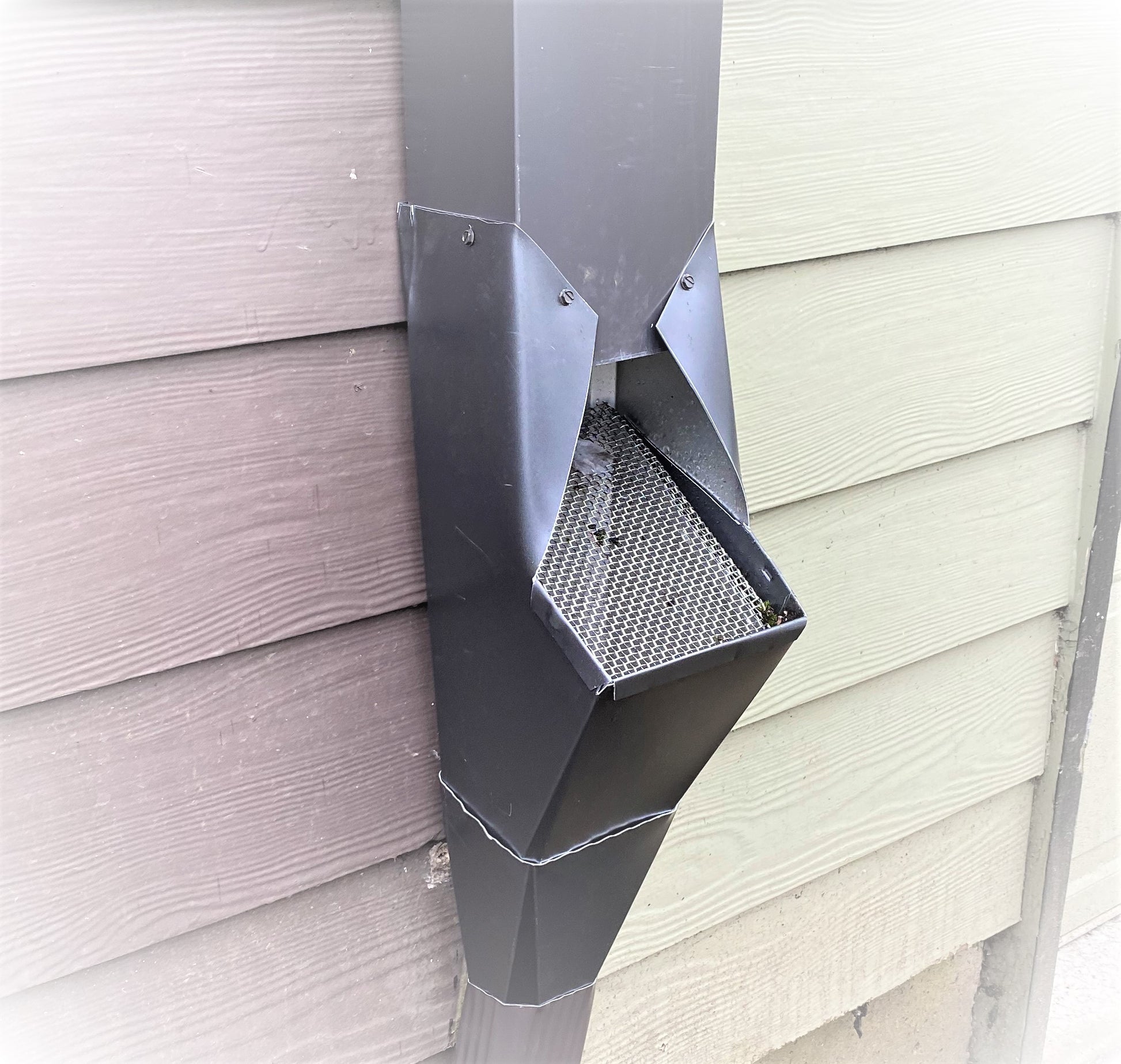 Black GutterAll downspout cleanout screen installed on a house wall.