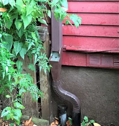 Brown GutterAll downspout cleanout screen installed near a red house wall.