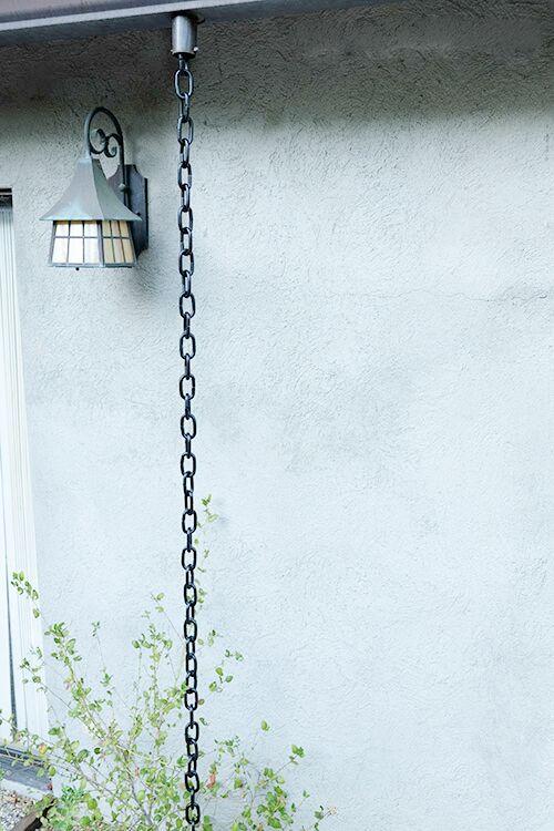 Full view of black aluminum rain chain hanging from a roof with a lantern nearby.