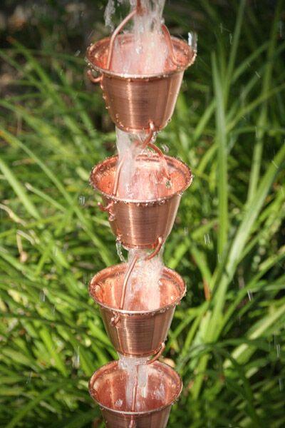 Copper rain chain with multiple bucket cups, water cascading in garden.