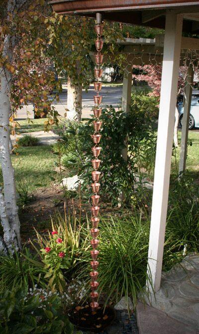 Full-length copper bucket cup rain chain installed in outdoor garden.