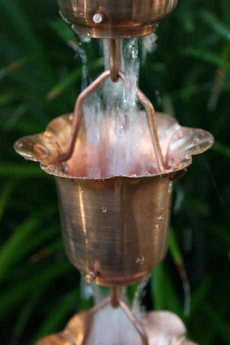 Copper-toned buttercup rain chain with water cascading through the cups.
