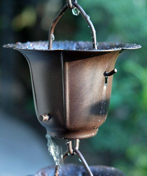 Dark bronze buttercup rain chain cup outdoors with water dripping.