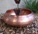 Copper rain chain basin placed outdoors with natural patina accents.