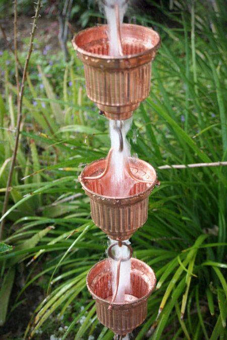 Copper rain chain with multiple cups and water cascading in a garden.