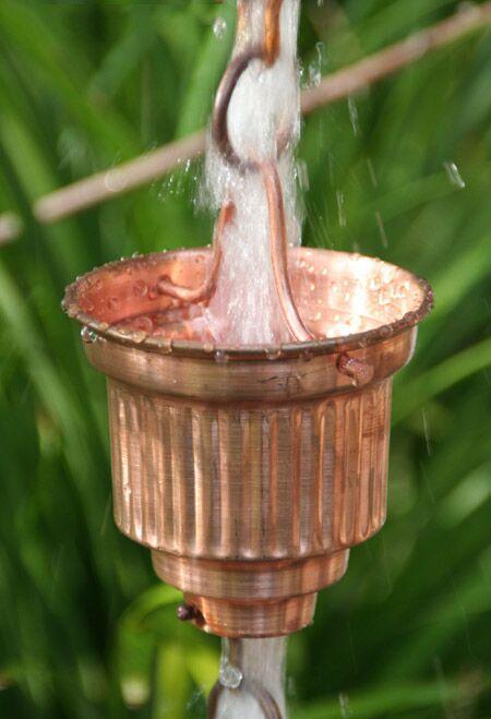 Detailed view of water flowing through a single copper rain chain cup.