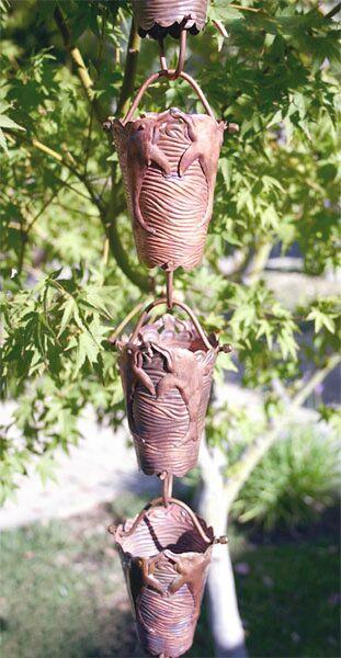 Full view of copper rain chain with dolphin design hanging in a garden.