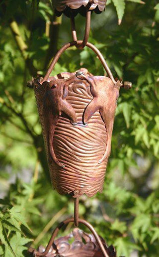 Copper rain chain with dolphin design hanging outdoors in a garden.