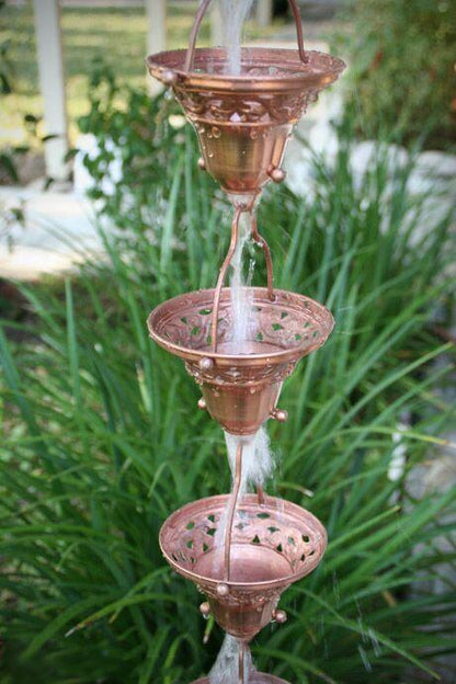Three-tiered copper floral bell cup rain chain with water flowing through.