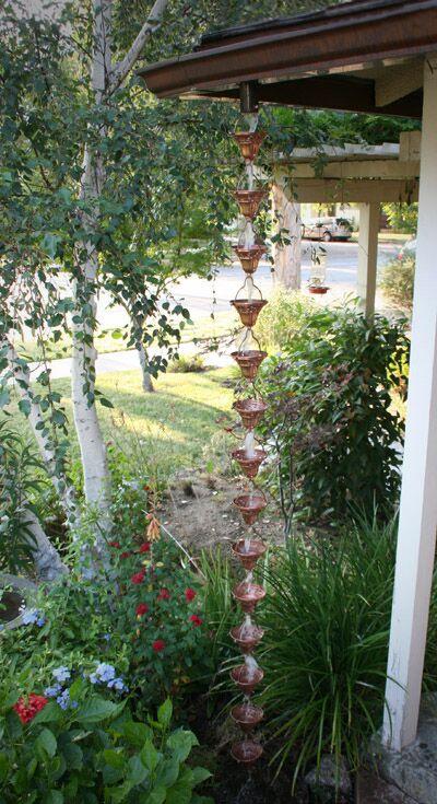 Full-length copper floral bell cup rain chain installed in a garden setting.