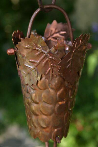 Detailed view of a handcrafted copper grapevine rain chain cup with leaf accents.