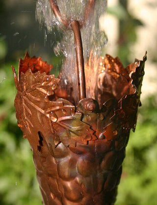 Copper grapevine rain chain cup with water flowing through, showcasing its functionality.