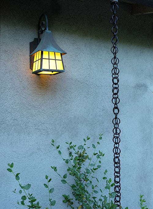 Black hooked rings rain chain installed near a lit outdoor lantern.
