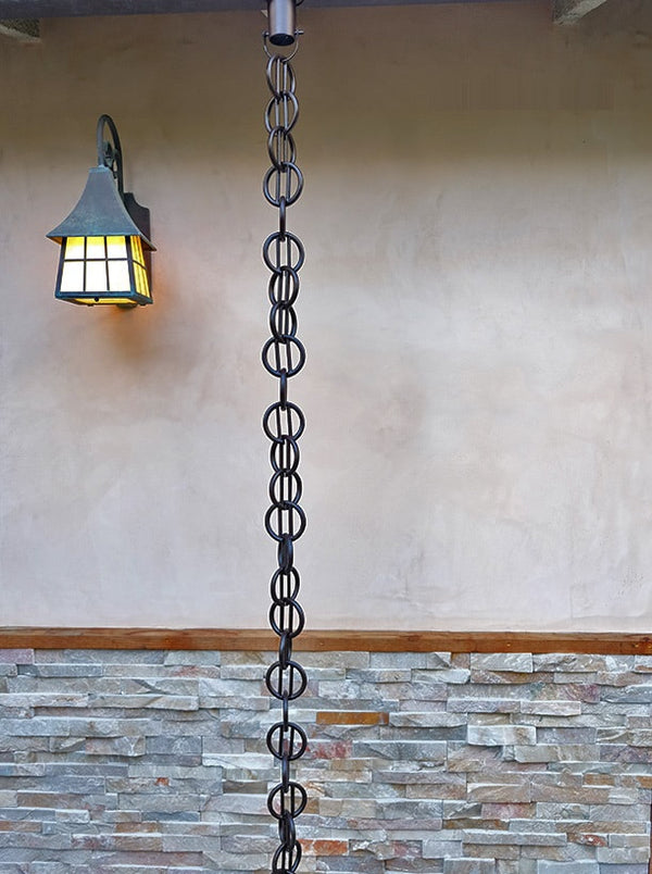 Black rain chain hanging from a house, serving as a stylish downspout alternative.