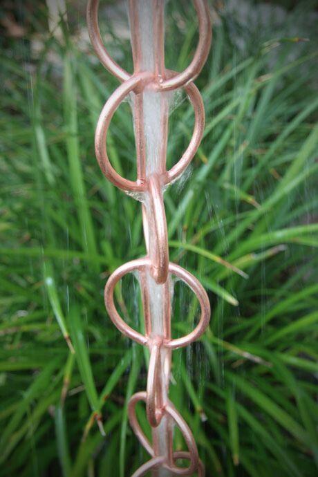 Copper rain chain with water flowing through geometric rings.