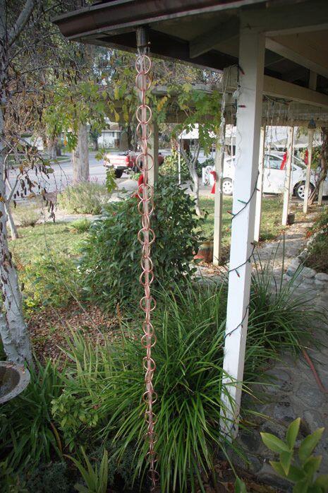 Copper rain chain installed in a garden setting as a downspout alternative.