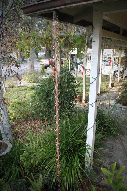 Copper rain chain installed in a garden setting as a downspout alternative.