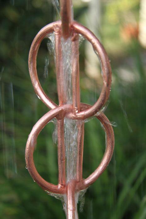 Close-up of copper rain chain with water cascading through rings.
