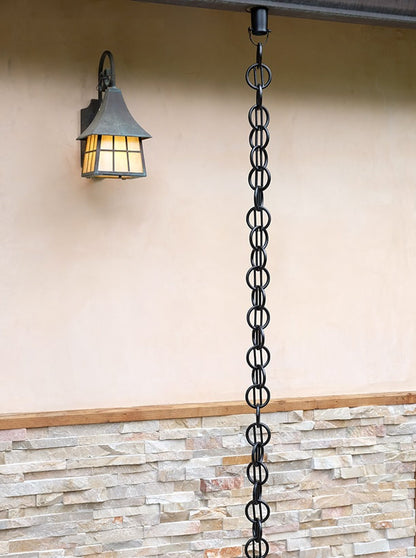 Black rain chain installed on a house with a modern geometric design.