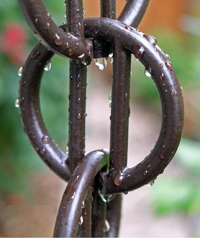 Close-up of black rain chain with water droplets on its rings.