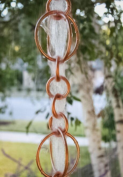 Copper rain chain with water cascading through hoops outdoors.