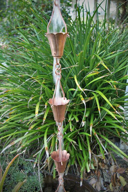 Handcrafted tulip copper rain chain with multiple cups in a garden setting.