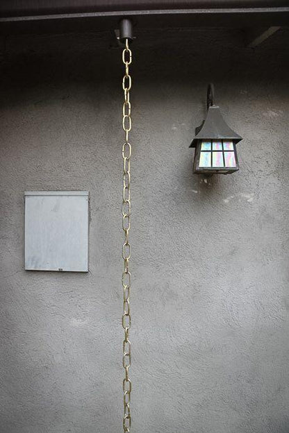Long brass link rain chain installed as a decorative downspout feature.