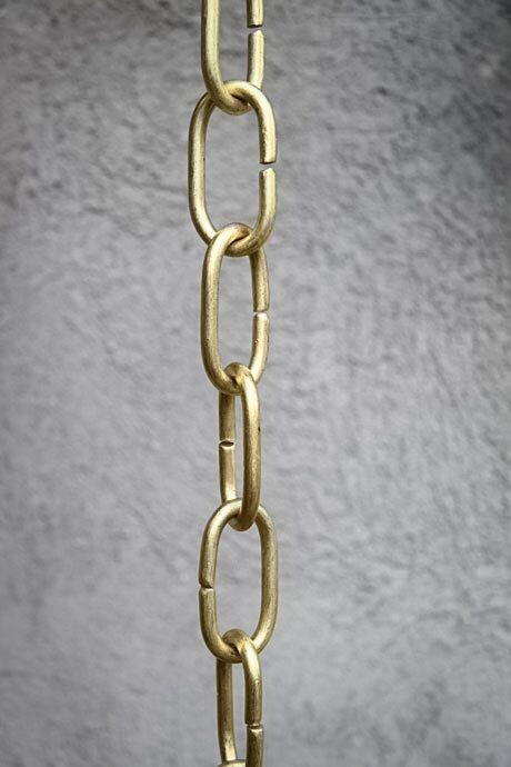 Handcrafted brass rain chain with long links against a textured wall.