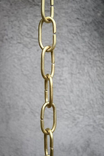 Handcrafted brass rain chain with long links against a textured wall.
