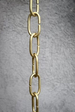 Handcrafted brass rain chain with long links against a textured wall.