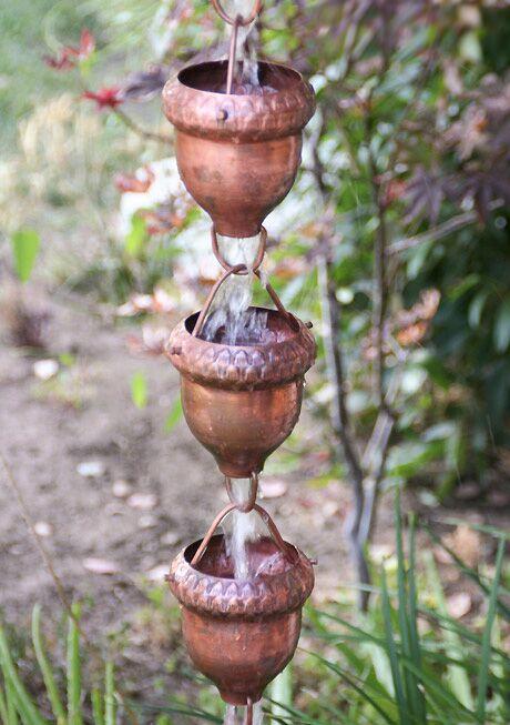 Decorative copper oaknut rain chain with water flowing in a garden setting.
