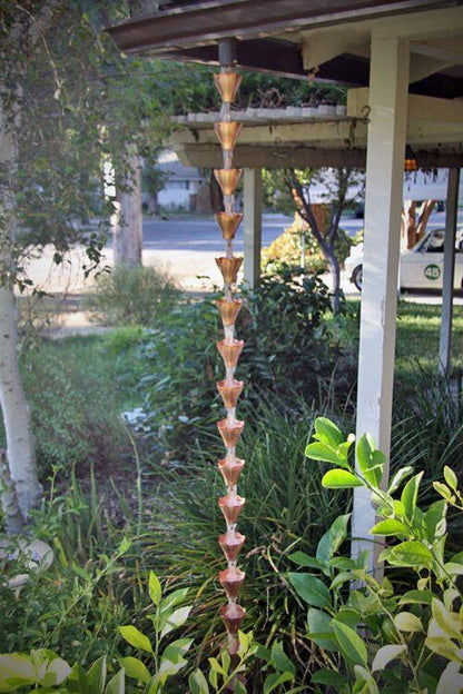 Full-length copper bloom cup rain chain installed in a lush garden.