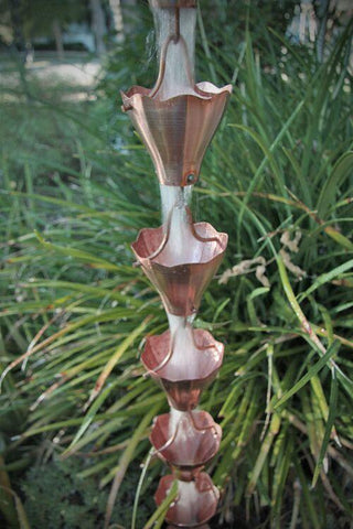 Decorative copper rain chain with multiple bloom cups in a garden setting.