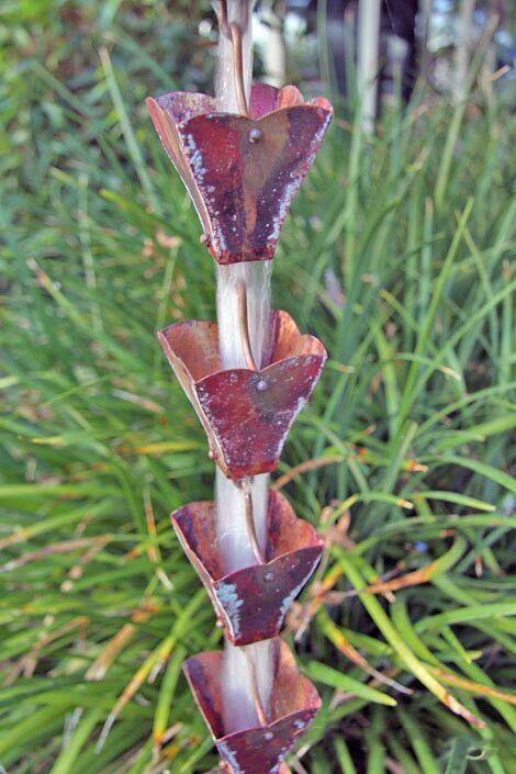 Decorative copper rain chain with petal top cups in a garden setting.