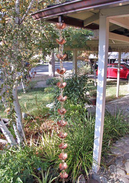 Full view of pink lotus copper rain chain hanging from a roof in a garden.
