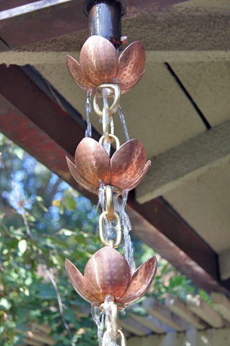 Pink lotus copper rain chain attached to a downspout with water flowing through.
