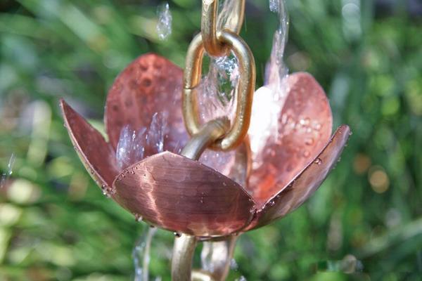 Water flowing through pink lotus copper rain chain in garden setting.