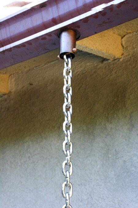 Polished stainless steel chain attached to a gutter for rain management.