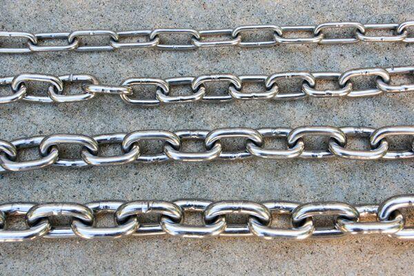 Multiple polished stainless steel chains displayed on a concrete surface.