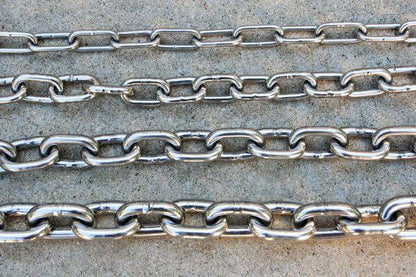 Multiple polished stainless steel chains displayed on a concrete surface.