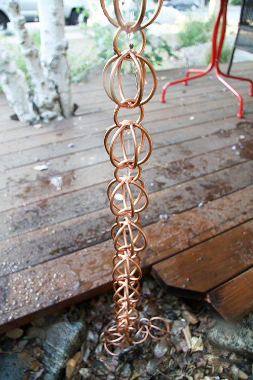 Copper rain chain installed on a wooden deck with water flow.