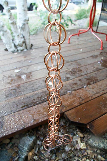 Copper rain chain installed on a wooden deck with water flow.