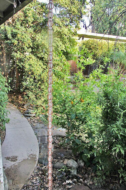 Full-length copper rain chain in a garden setting with lush greenery.