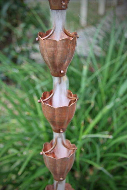 Multiple copper funnel cups forming a rain chain with water flowing.