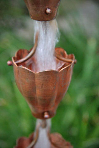 Decorative copper rain chain funnel cup with water cascading outdoors.