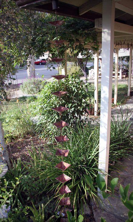 Full view of a shallow square cup rain chain installed on a porch, surrounded by greenery.